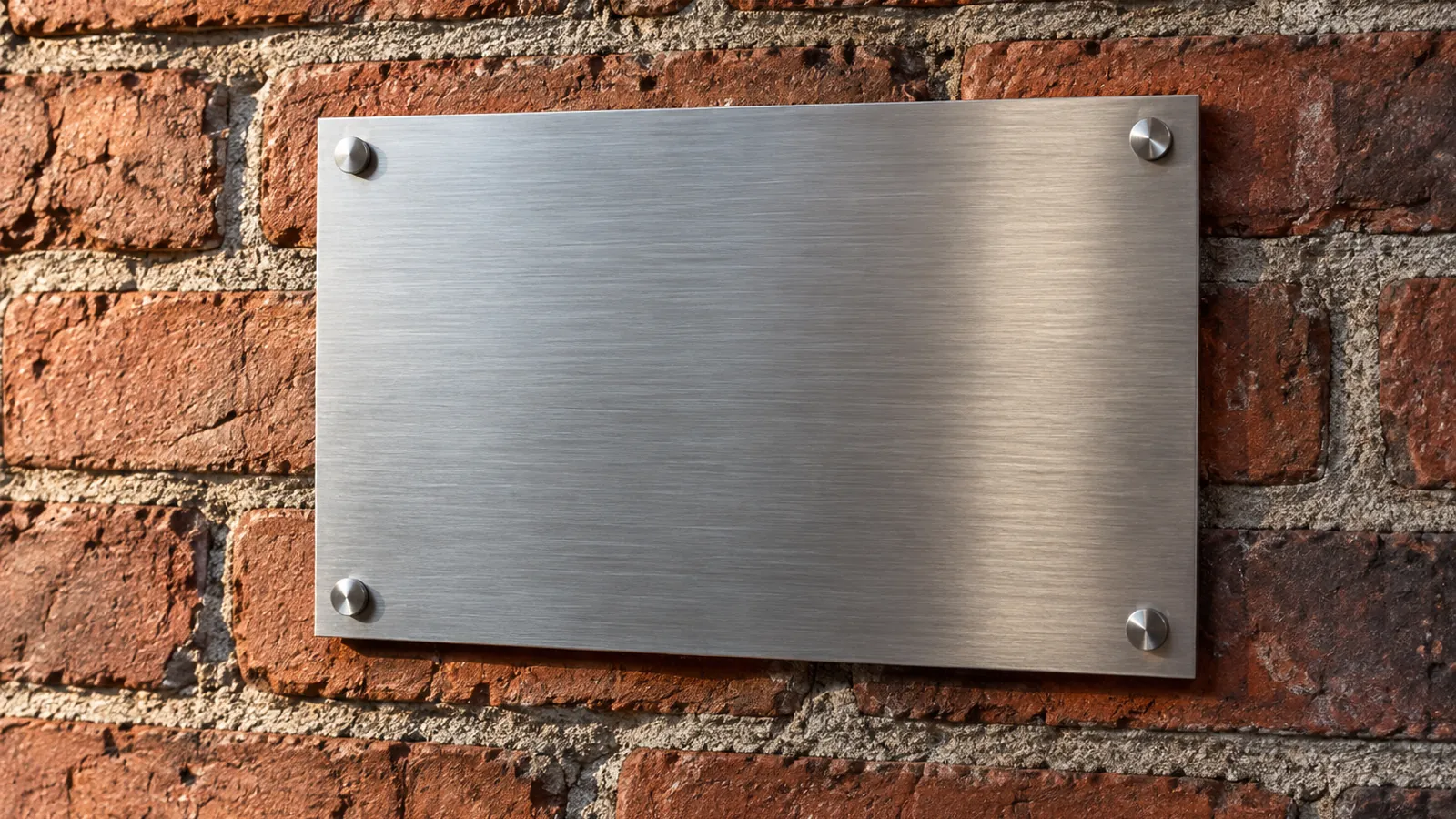 A blank unengraved brushed stainless plaque mounted on a red brick wall